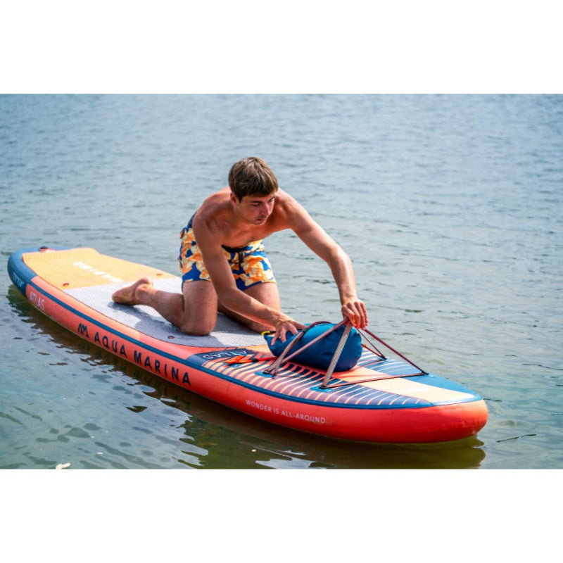 Man Putting Bag Under Bungee Strap on Aqua Marina Atlas SUP on Water