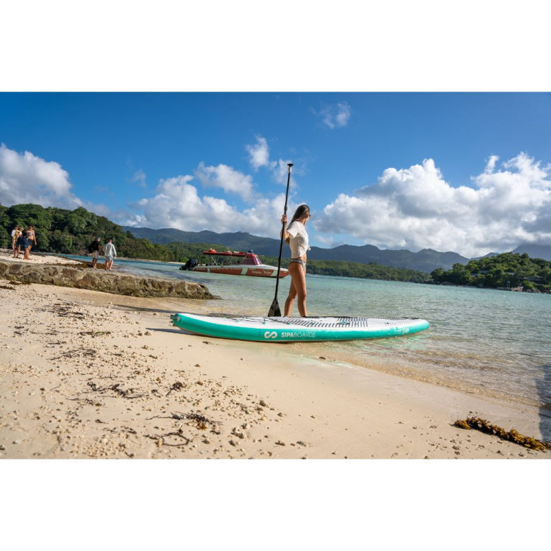Woman Holding Paddle Walking into Ocean with Sipaboards Drive Tourer Electric SUP on Beach Next to Her