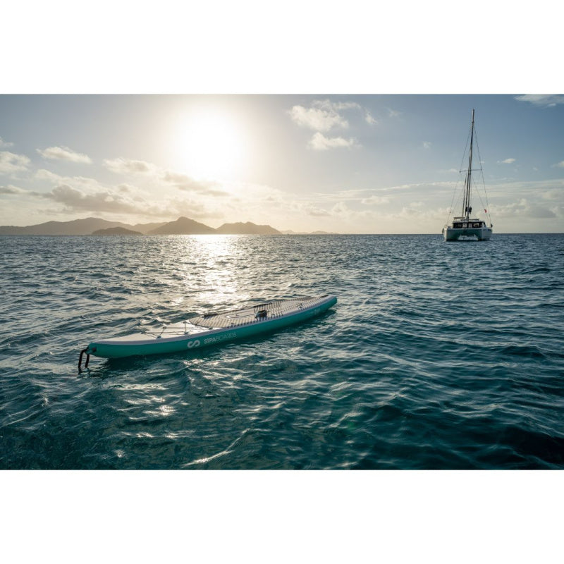 Sipaboards Drive Tourer Electric SUP in Ocean with Sailboat, Mountains, and Sun in the Background
