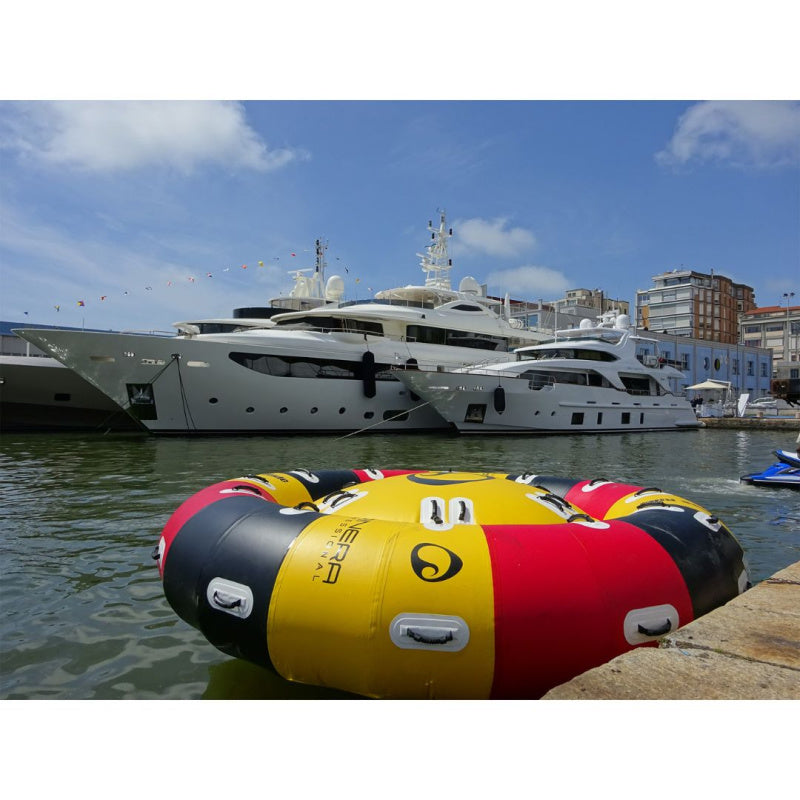 Spinera Professional Endless Ride 4-6 Person Towable Tube in Black, Yellow & Red in Water Along Dock with Superyachts in Back